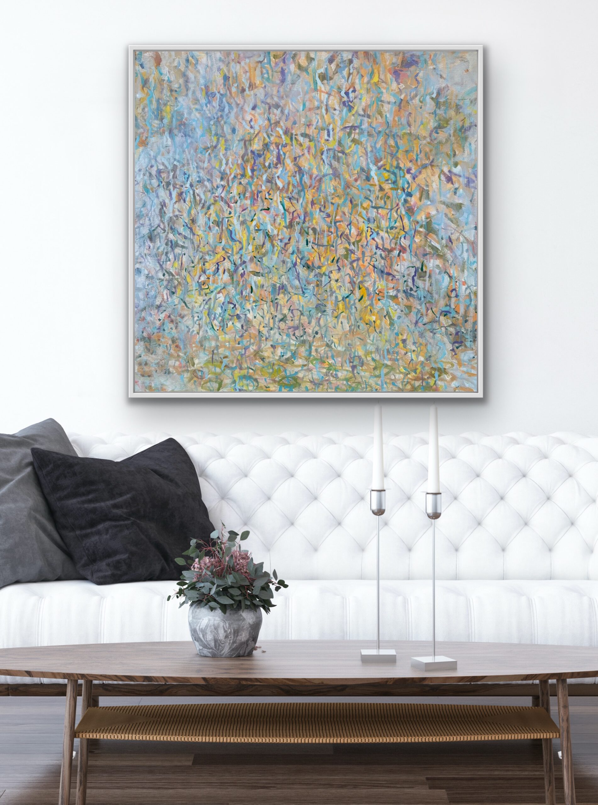 Elegant white tufted sofa with black cushions and floral painting above.